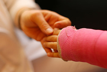 Kinderarm mit Gips in rosa und größere Hand in der Kinderchirurgie Rostock
